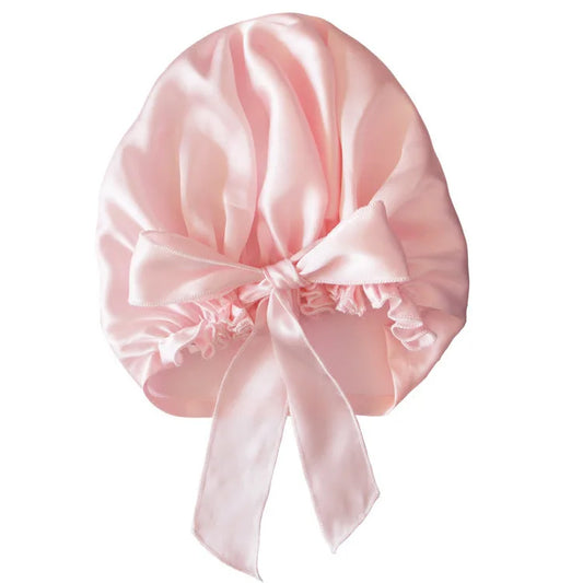 Pink satin bonnet with a bow, designed for hair protection during sleep, on a white background.